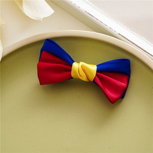 Detail of red, blue, and yellow satin ribbon bow hair clip on a green matte tray