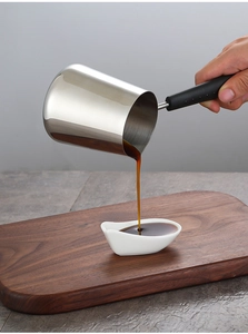 Close-up of stainless steel milk pan pouring dark liquid into a white ceramic cup