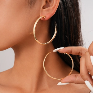Close-up of a large golden geometric hoop earring on a model with metallic finish