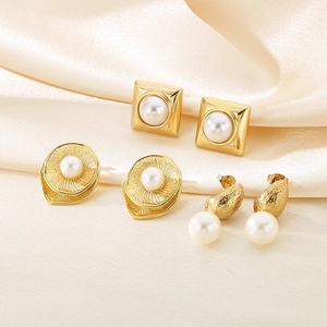 Three pairs of elegant gold titanium steel earrings with pearl accents on silk background