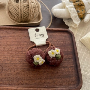 Detailed close-up of brown knitted hair ties with embroidered flowers on a wooden tray