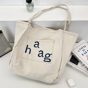 Close-up of beige canvas tote bag with blue haag lettering pocket in lifestyle setting