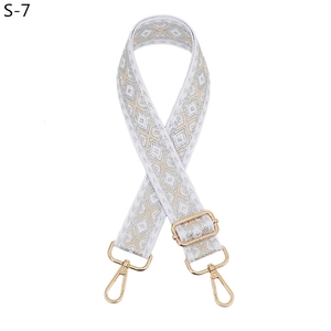 Detail of white geometric fabric shoulder strap with gold hardware hooks and buckle