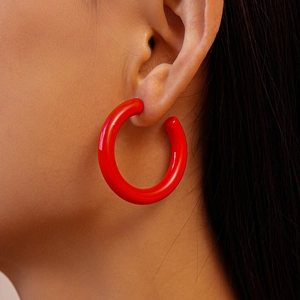 Gros plan d'un mannequin portant de grosses boucles d'oreilles créoles rouges en C en résine brillante