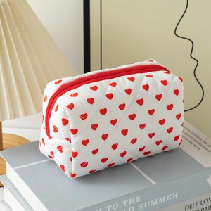 Close-up of a quilted cotton makeup bag with red heart patterns on a soft white base