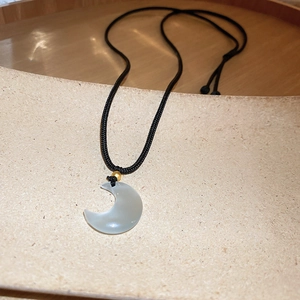 Detail shot of a crescent moon pendant with ice-white stone on black cord necklace