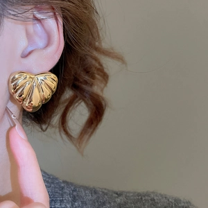 Close-up of golden heart earrings with textured leaf patterns on a model