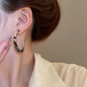 Macro side view of C-shaped resin earrings with marble pattern on a model's ear