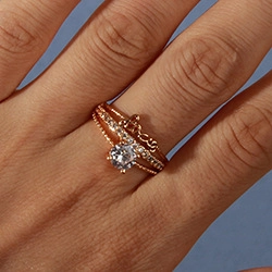 Close-up of gold-plated ring set featuring cursive design and sparkling clear gemstone