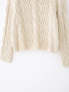 Detailed macro view of cable-knit textures and wavy vertical patterns on cream wool sweater
