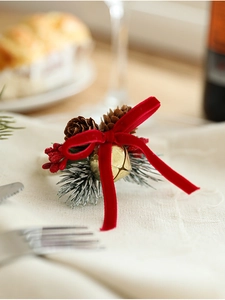 Detail of Christmas napkin ring with red velvet bow, gold bell, pine cone, and berries