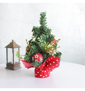 Close-up of a mini Christmas pine tree with red ornaments and a burlap base