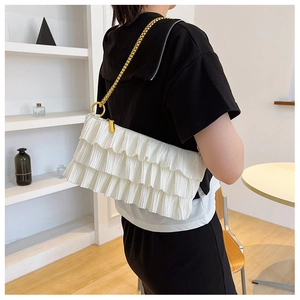 Close-up of pleated white shoulder bag with golden chain strap and ruffled design