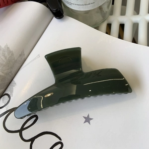 Detail of dark green glossy hair claw clip placed on a white magazine with glass decor