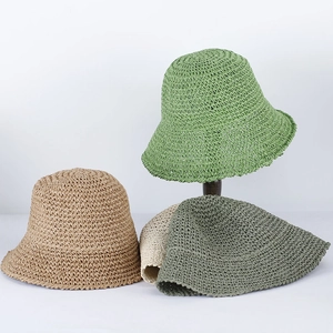 Close-up detail of woven straw bucket hats in green and khaki on a wooden stand