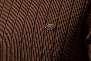 Close-up of brown ribbed knit sweater with metal brand logo plaque on the fabric
