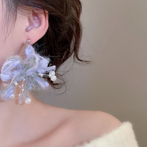 Close-up of fuzzy knit flower earrings with pearls worn by a model in soft lighting