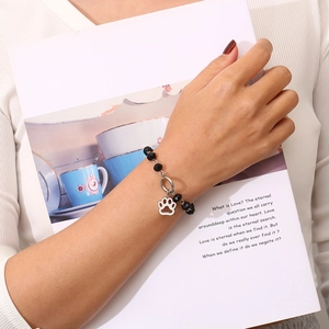Detail of beaded bracelet featuring a silver hollow cat paw pendant on a wrist