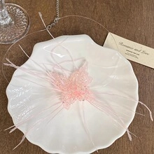 Dettaglio della collana a farfalla rosa con piume in un piatto a forma di conchiglia