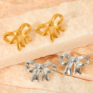 Macro view of gold and silver bow stud earrings on a textured stone background