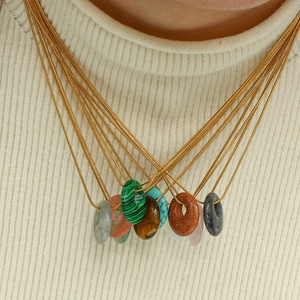 Close-up of layered gold necklaces featuring malachite and agate stone circle pendants