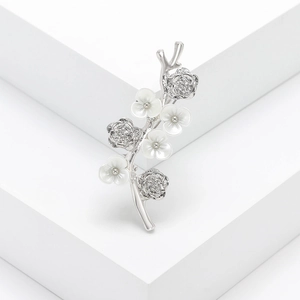 Elegant silver flower branch brooch with white petals and rhinestones on a white podium