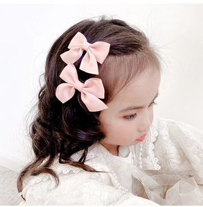 Détail de deux barrettes à nœuds roses portées par une petite fille en robe dentelle
