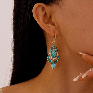 Detail of bohemian gold drop earrings with turquoise stone and blue beaded fringe