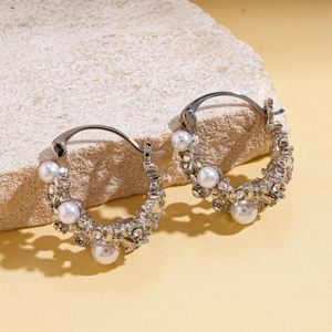 Detailed view of C-shaped silver earrings with pearls and crystals on stone background