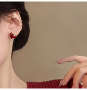 Detail of a red dragon stud earring with gold plating worn by a model in a close-up view