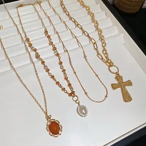 Four gold layered necklaces featuring acrylic pearls and a textured cross pendant