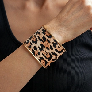 Detail of wide leopard print bangle with gold trim worn on a wrist against a black top