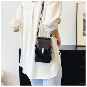 Détail d'un sac à bandoulière noir en similicuir avec une boucle argentée en forme de U