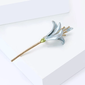 Detail of light blue enamel lily brooch with gold accents and green sepals on white stand