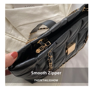 Close-up of smooth gold metal zipper and chain strap on black quilted tote bag