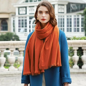 Solid orange cashmere-feel scarf with fringes worn over a blue coat for winter warmth