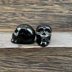 Detailed view of two polished black obsidian crystal skulls on a dark wood background