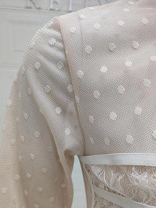 Detailed view of beige dress with polka dot mesh, lace trim and white leather straps
