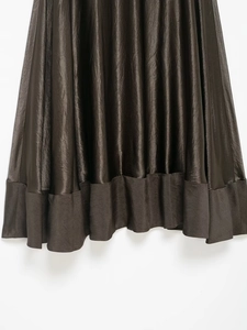 Détail de l'ourlet de la jupe en satin marron foncé avec texture lisse et beau drapé