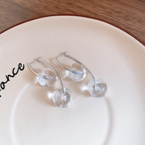 Detail of silver cherry drop earrings featuring transparent glass spheres on a ceramic plate
