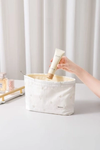 Detail of white striped makeup bag with bear embroidery and zip closure in use