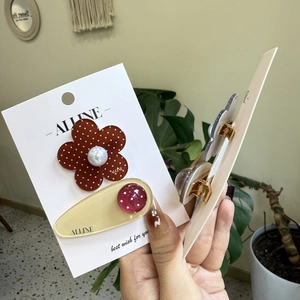 Detail view of oval polka dot hair clip and brown floral clip with pearl accent