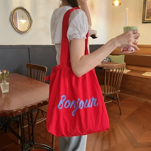 Detail of red canvas tote bag with Bonjour print worn by model in a cozy cafe setting