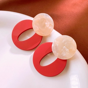 Detail of red and beige geometric acrylic earrings on a white ceramic plate