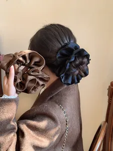 Macro detail of large ruffled silk-like scrunchies in black and brown satin texture