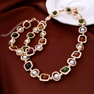 Détail d'un collier vintage doré avec perles blanches et pierres vertes sur soie