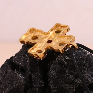 Macro shot of 18K gold-plated cross pendant with colorful gems on volcanic rock