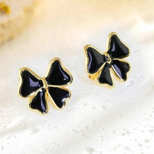 Macro shot of gold-plated bow earrings with black enamel drip finish on white stone