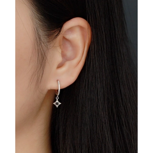 Detailed view of silver hoop earring with black gemstone cross pendant on a model's ear