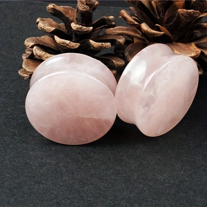 Macro detail of natural pink quartz stone ear tunnels on a dark textured background